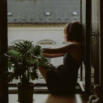 cô gái ngồi bên cửa sổ với cây cảnh nghĩ về năng suất độc hại