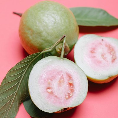 Trái ổi ruột hồng và lá ổi tươi đặt trên nền hồng – minh họa tác dụng của lá ổi đối với sức khỏe và sắc đẹp.
