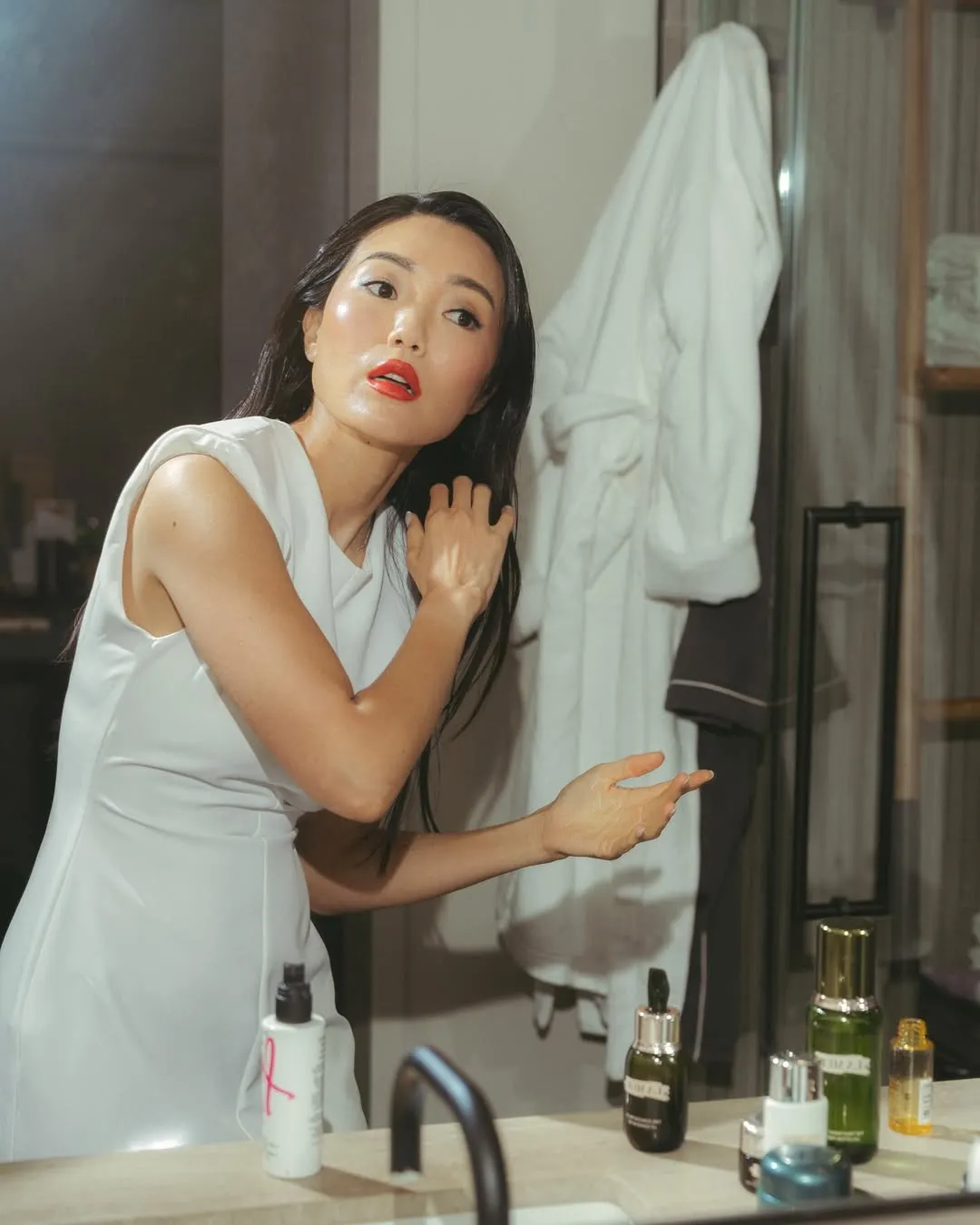 Người phụ nữ châu Á đang chăm sóc tóc và da trước gương trong phòng tắm