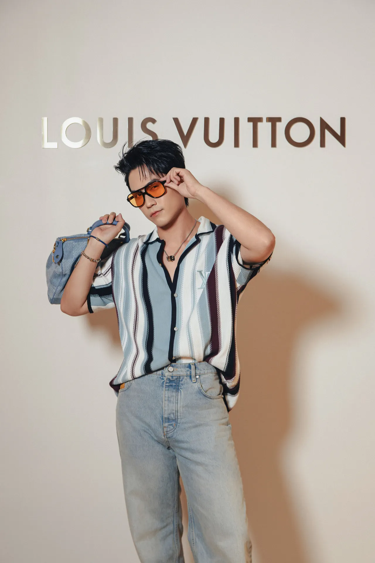 Võ Điền Gia Huy trẻ trung trong thiết kế sơ mi ngắn tay kẻ sọc và quần jeans sáng màu đi kèm túi xách chất liệu denim monogram.