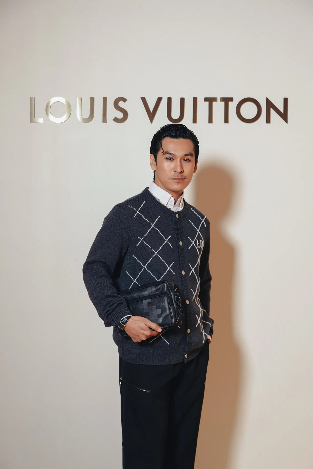 Thiên Minh lịch lãm trong áo khoác len họa tiết caro đen xám và quần tây đen đi kèm túi đeo chéo nhỏ gọn cùng tông.