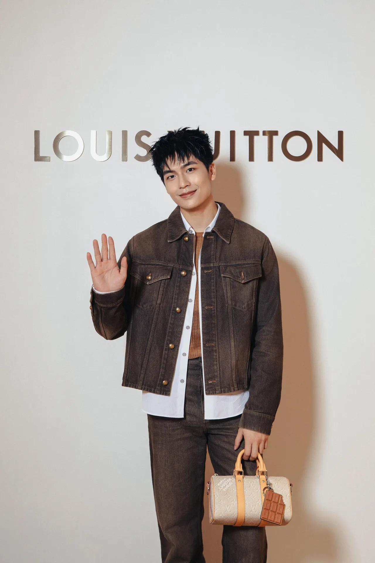 Trần Quốc Anh diện áo khoác denim nâu cùng quần ống rộng, đi kèm túi Speedy và phụ kiện charm hình thanh chocolate.