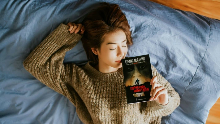 Cô gái cầm sách nằm trên giường trong giấc ngủ