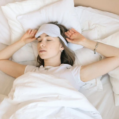 Người phụ nữ đang ngủ yên giấc với bịt mắt trên giường, tạo tư thế nghỉ ngơi thoải mái giúp hạn chế ngáy ngủ.