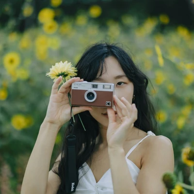 Cô gái gen Z cầm máy ảnh kỹ thuật số chụp ảnh giữa vườn hoa cúc vàng