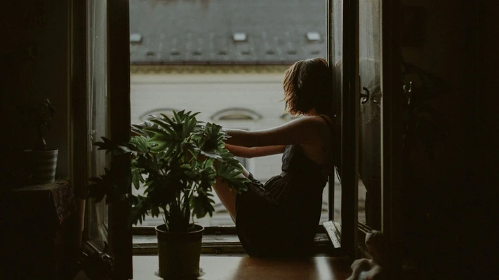 cô gái ngồi bên cửa sổ với cây cảnh nghĩ về năng suất độc hại
