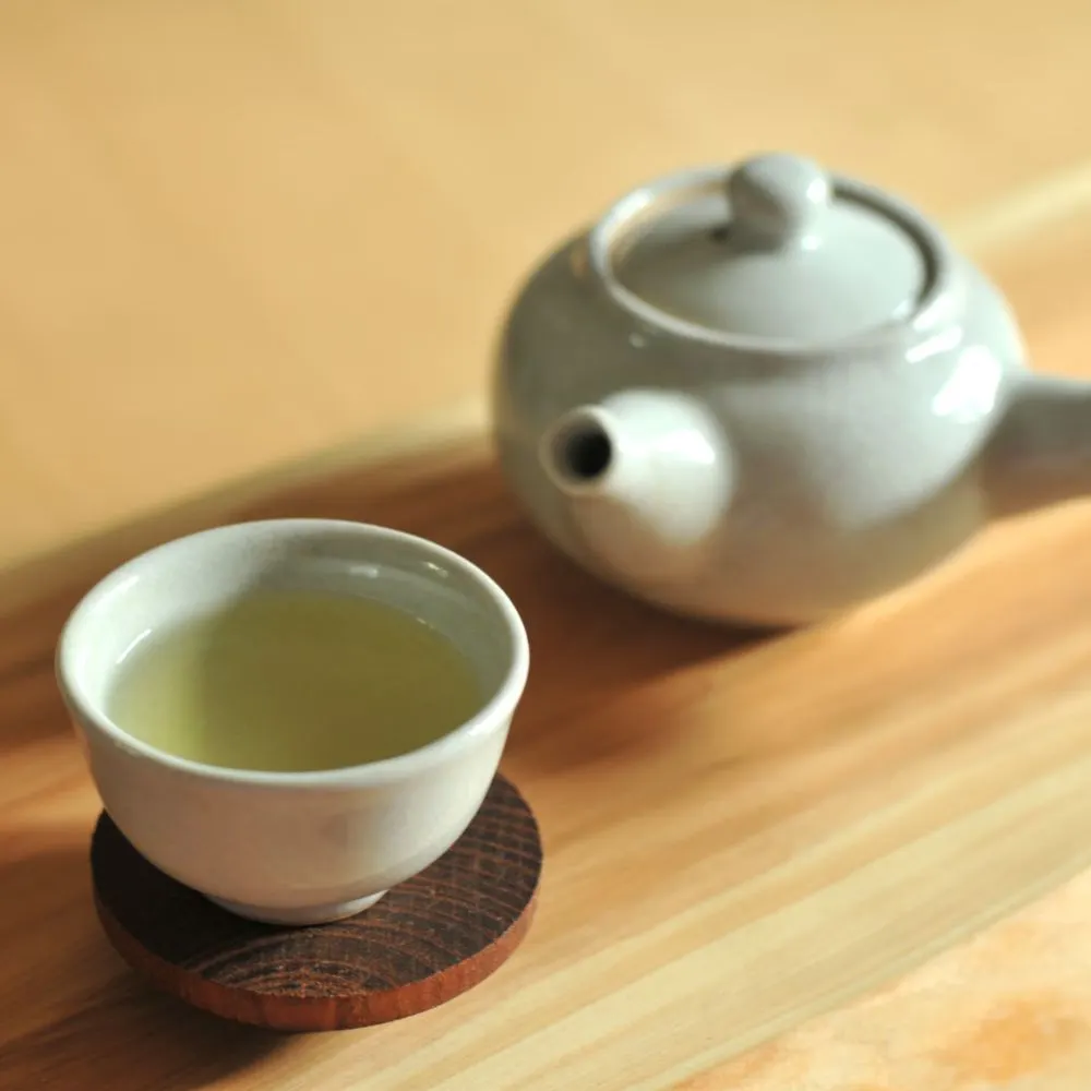 Tách trà xanh và ấm trà nhỏ bên cạnh.