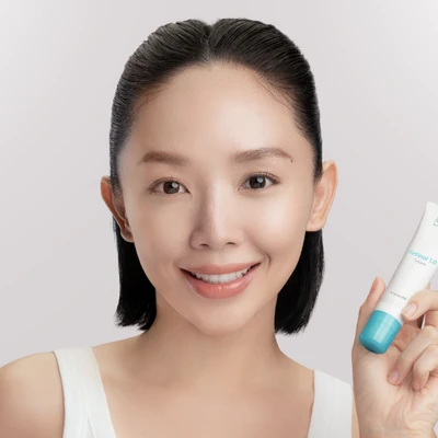 Obagi - ca sĩ Tóc Tiên mặc áo tank top màu trắng, buộc tóc nửa đầu, tay cầm tuýp kem dưỡng retinol của Obagi và nhìn chính diện vào camera để chụp ảnh chân dung
