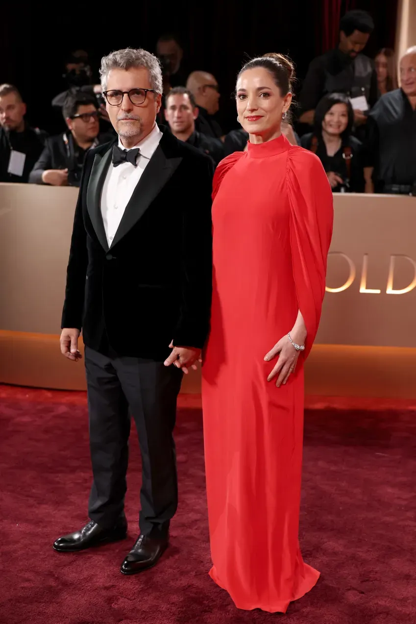 Kleber Mendonça Filho xuất hiện trong bộ tuxedo nhung đen sang trọng kết hợp cùng đồng hồ Cartier Tank Américaine, sánh bước bên Emilie Lesclaux quyến rũ trong thiết kế đầm đỏ rực rỡ kết hợp hoa tai Reflection và vòng tay Panthère de Cartier đính kim cương, ngọc lục bảo.