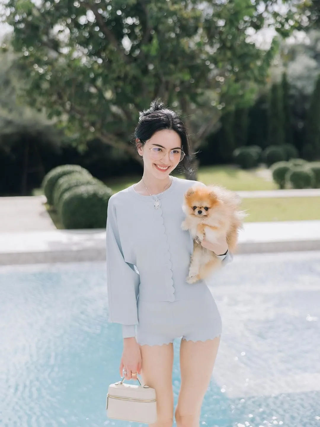 Mai Davidka mặc đồ màu xanh nước biển nhạt, ôm thú cưng, cười tươi, hàm răng trắng sáng