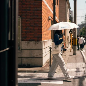 Một cô gái Nhật đi bộ trên vỉa hè trong trang phục thoải mái, che ô trắng dưới trời nắng