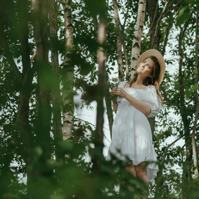 Cô gái đầm trắng ngắn đội mũ dựa gốc cây yêu thương bản thân