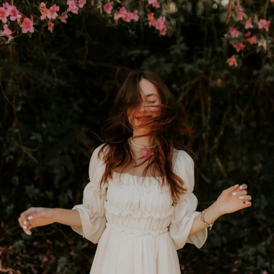 cô gái cung hoàng đạo tháng 12/2025 xõa tóc mỉm cười đứng dưới tán cây hoa