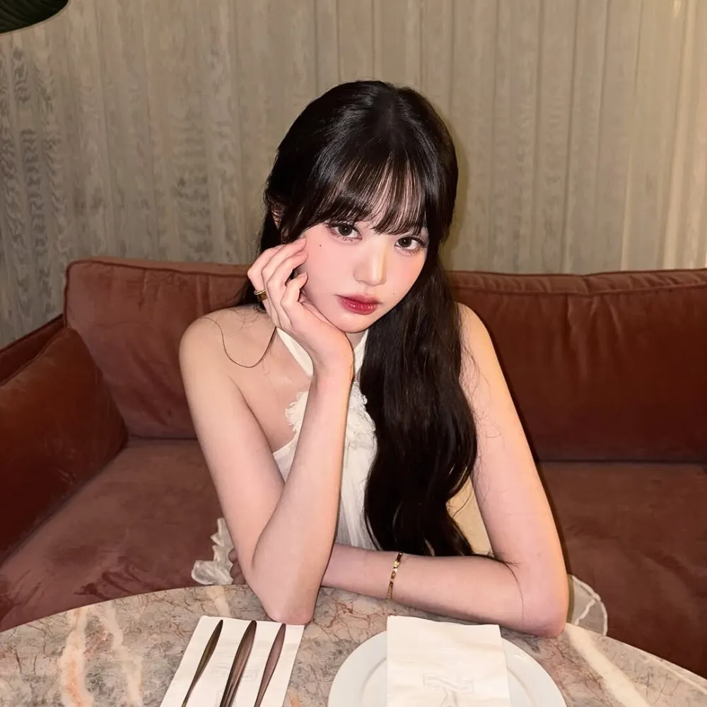 Jang Won Young ngồi chống tay lên cằm và thoa màu son đỏ hồng hợp trang phục trắng