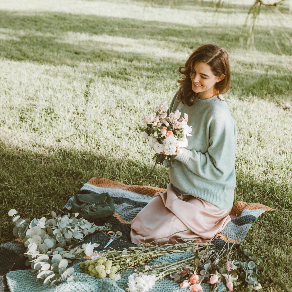 Cô gái ngồi trên bãi cỏ cắt tỉa bó hoa có dấu hiệu cuốn hút