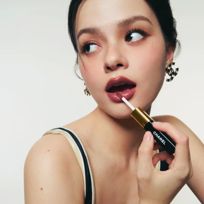 Rebecca “Becky” Patricia Armstrong thoa son Chanel Le Rouge Duo Ultra Tenue sắc Intense Caramel, ánh nhìn quyến rũ, diện khuyên tai logo Chanel.