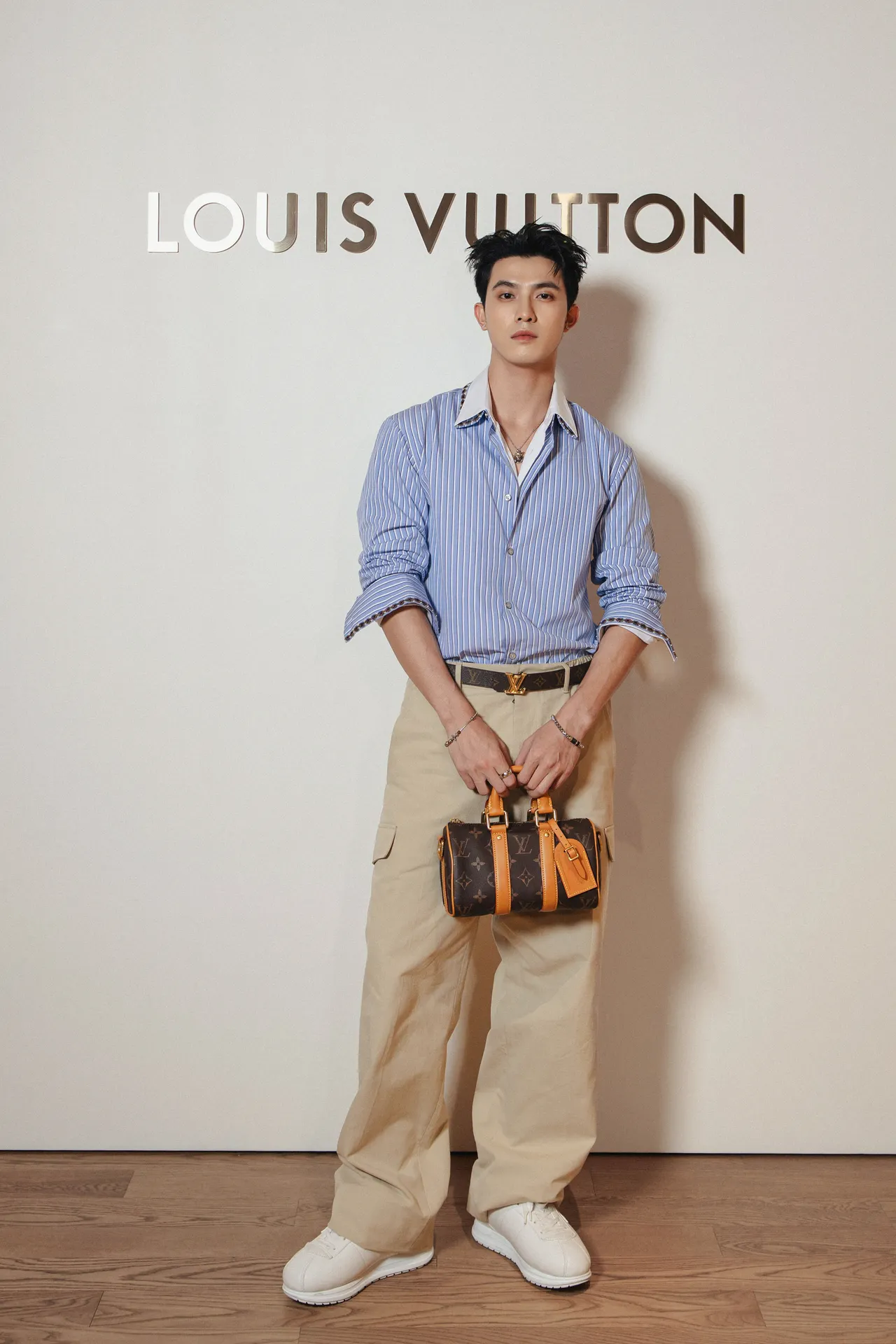 Trần Ngọc Vàng phối hợp sơ mi kẻ sọc xanh với quần cargo màu be hoàn thiện vẻ ngoài bằng thắt lưng monogram và giày sneakers trắng tối giản.