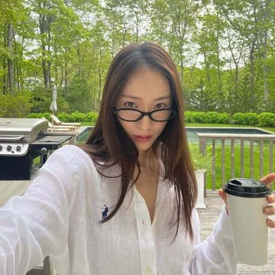 KRYSTAL JUNG mặc sơ mi trắng, cầm cốc sinh tố protein giữa khung cảnh thiên nhiên xanh mát