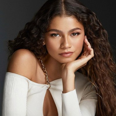 Zendaya mang áo tay dài màu trắng đang chống một tay lên cằm