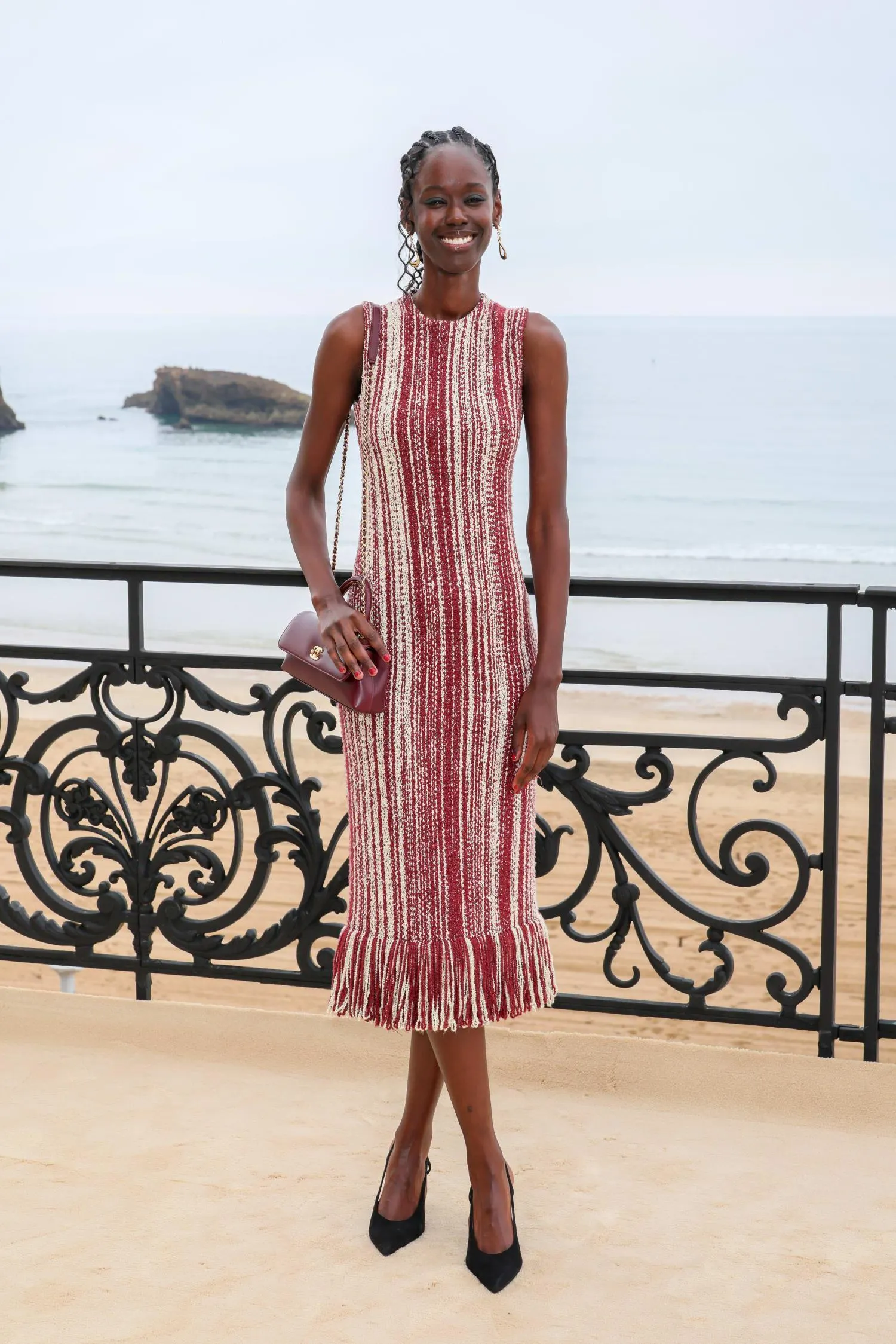 chiếc đầm len dệt kim dáng ôm với họa tiết sọc đỏ – trắng mang lại cảm giác thủ công tinh xảo. Thiết kế sát cơ thể, phần gấu tua rua nhẹ, được kết hợp cùng giày cao gót mũi nhọn và túi đeo vai nhỏ, tạo nên vẻ nữ tính nhưng vẫn năng động.