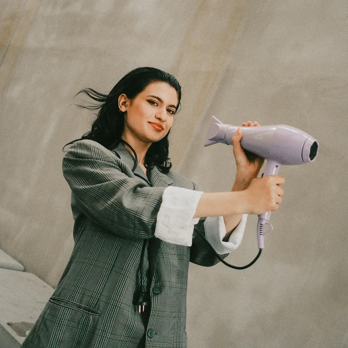 Cô gái xõa tóc mặc áo vest cầm máy sấy tóc