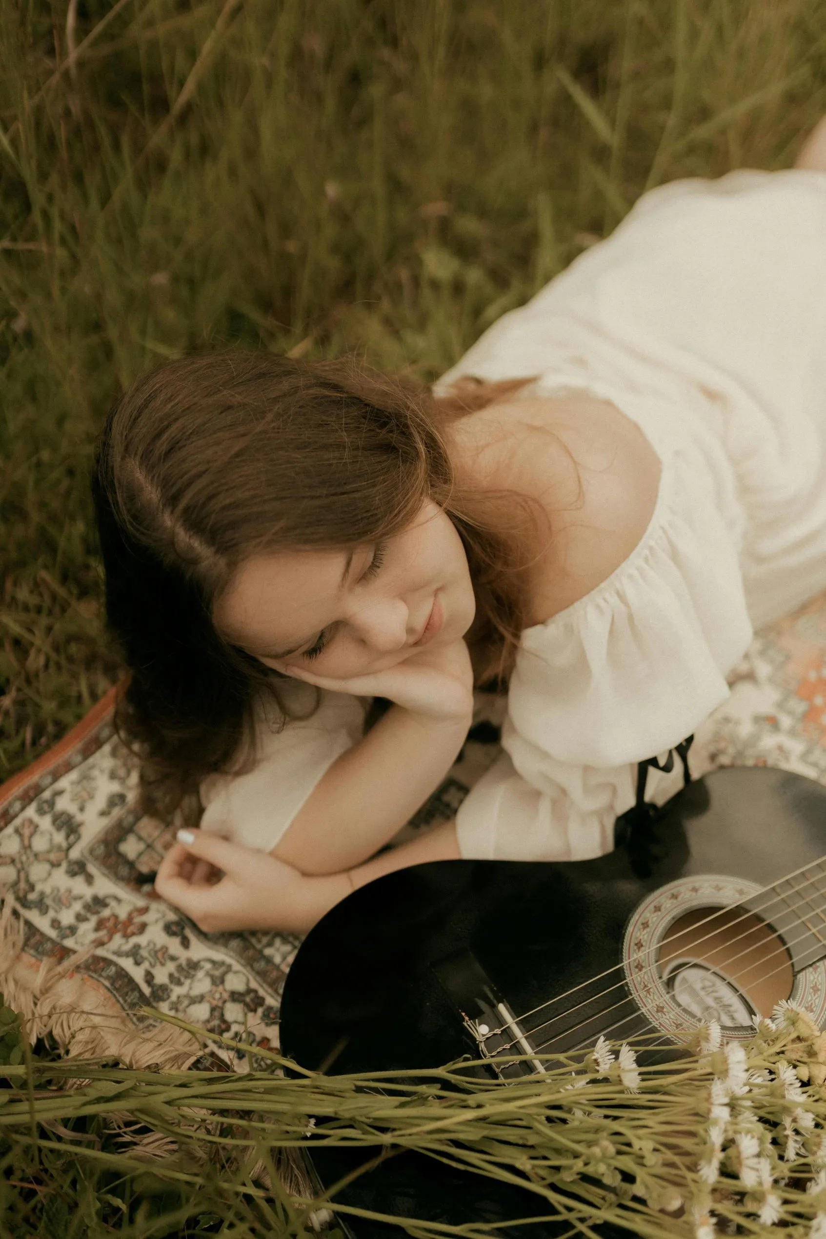 cô gái mặc váy trễ vai trắng tay chống cằm nằm trên bãi cỏ xanh