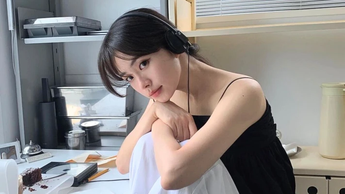 cô gái đeo tai nghe đang ngồi khoanh hai tay lên đầu gối